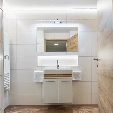 A modern bathroom with wood and tile accents. The space is bright and designed in a minimalist style, featuring a sink and a large mirror.