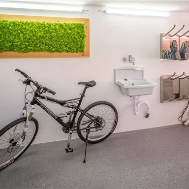 Eine moderne Fahrradgarage mit einem schwarzen Mountainbike. An der Wand sind ein Waschbecken und Halterungen für weiteres Zubehör zu sehen.