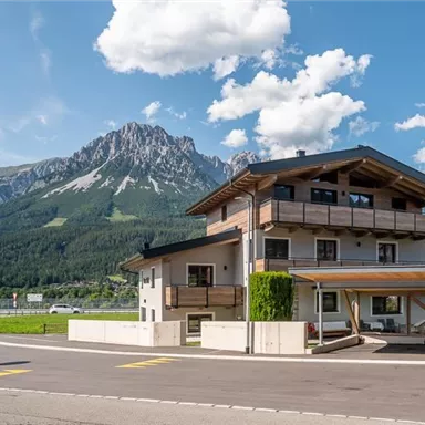 Ein modernes Gebäude inmitten einer malerischen Berglandschaft. Die Umgebung ist grün und die Wolken über den Bergen sind klar sichtbar.