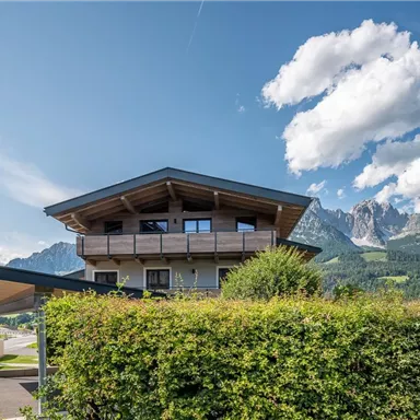 Ein modernes Gebäude mit einem gebogenen Dach und großen Fenstern. Im Hintergrund sind majestätische Berge und ein klarer blauer Himmel zu sehen.