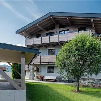 Ein modernes Haus in den Bergen mit einem begrünten Garten. Der klare Himmel und die umliegende Landschaft schaffen eine einladende Atmosphäre.