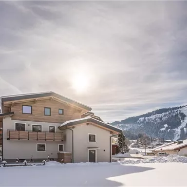 Ein modernes Haus in einer verschneiten Landschaft. Die Sonne scheint über den Bergen und dem schneebedeckten Boden.