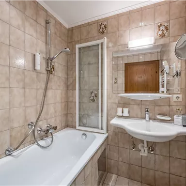 Ein Badezimmer mit einer Badewanne und einer Duschkabine. Die Wände sind mit hellen Fliesen dekoriert und es gibt ein Waschbecken mit einem Spiegel.