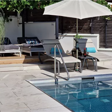 A relaxing pool area with loungers and a sun umbrella. The surroundings are green and inviting, perfect for relaxation.