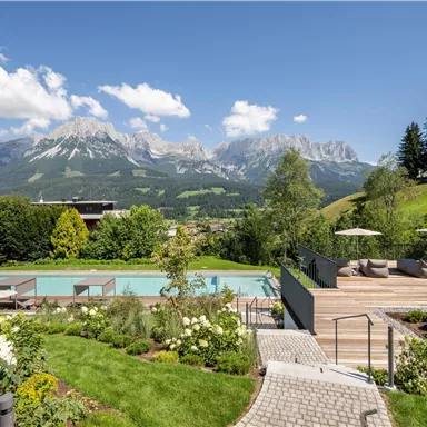 Ein schöner Außenbereich mit einem Pool und Blick auf majestätische Berge. Umgeben von grünen Wiesen und blühenden Pflanzen ist es ein perfekter Ort zum Entspannen.