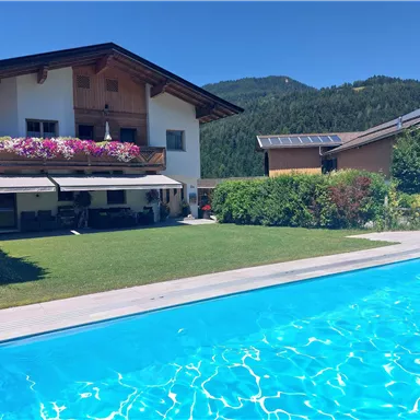 Ein schönes Haus mit einem Pool und gepflegtem Garten. Die Umgebung ist von Bergen und Sonnenlicht umgeben.