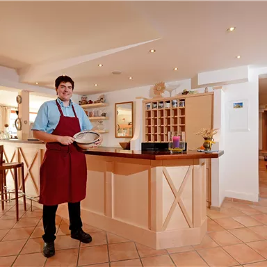 Ein freundlicher Kellner steht an einer hellen Theke in einem Restaurant. Die Einrichtung ist modern und einladend.