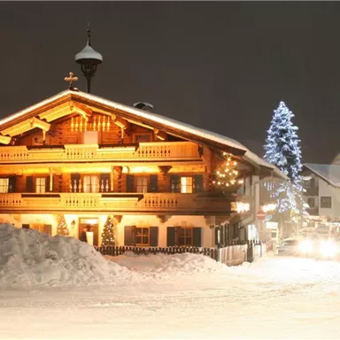 Ein charmantes Holzhaus im Winter mit warmem Licht. Der schneebedeckte Boden und ein beleuchteter Weihnachtsbaum schaffen eine festliche Atmosphäre.