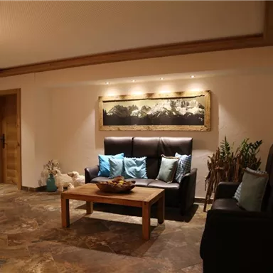 Ein gemütlicher Wohnbereich mit zwei Sofas und einem Holztisch. An der Wand hängt ein dekoratives Bild, und es ist sanft beleuchtet.