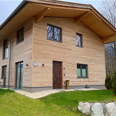 Ein modernes Holzhaus mit einer ansprechenden Fassade. Der Garten ist grün und gut gepflegt.