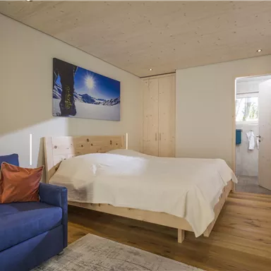 Ein gemütliches Schlafzimmer mit einem großen Bett und einer blauen Couch. An der Wand hängt ein Bild von einer schneebedeckten Landschaft.