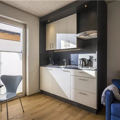 Eine moderne Küchenzeile mit hellen Möbeln und Kochgeräten. Daneben steht ein Tisch und ein Stuhl in einem freundlichen Raum.