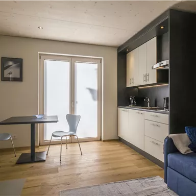 Eine moderne Küche mit einem Tisch und zwei Stühlen. Der Raum ist hell und einladend, mit einem gemütlichen Sofa und großen Fenstern.