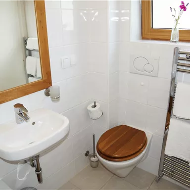 Ein modernes Badezimmer mit einer weißen Wandfliesen und einem Holzboden. Es verfügt über ein Waschbecken, eine Toilette und frische Handtücher.