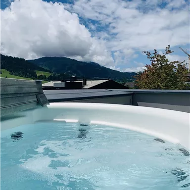 A whirlpool on a terrace overlooking green hills and mountains. The sky is clear with a few clouds.
