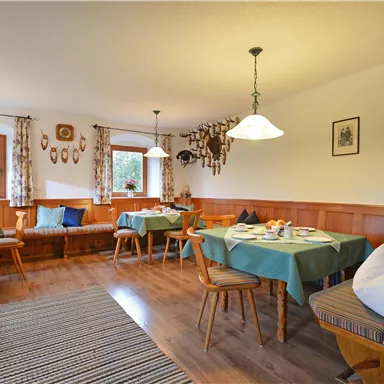 A cozy restaurant area with wood paneling and several tables. The light from the lamps and the window creates an inviting atmosphere.