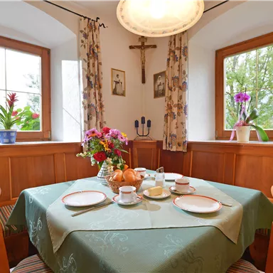 An inviting dining area with a table decorated with dishes and a flower centerpiece. The windows offer a view of the greenery, and the room has a warm, cozy atmosphere.