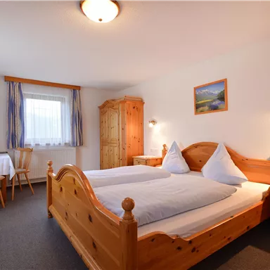 A cozy room with two wooden beds and blue decor. In the background, there is a table, chairs, and a small television.
