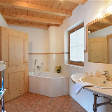 A modern bathroom with a wooden ceiling, bathtub, and sink. Fresh towels are neatly stacked and plants bring a touch of nature.