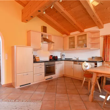 A modern kitchen with wooden ceilings and bright walls. The dining area is cozily furnished and offers plenty of light.