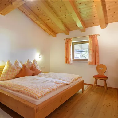 A cozy bedroom with a wooden ceiling and a large bed. There is a window, a television, and a wooden chair.