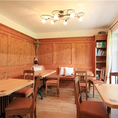 A cozy room with wood paneling and light tables. The windows are decorated with curtains, and shelves with books are visible.