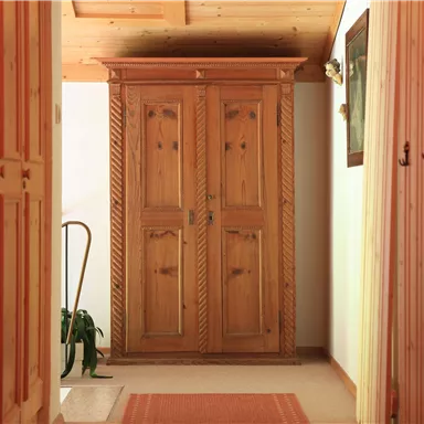 A hallway with a large wooden wardrobe. There are light doors on the walls and a carpet lies on the floor.