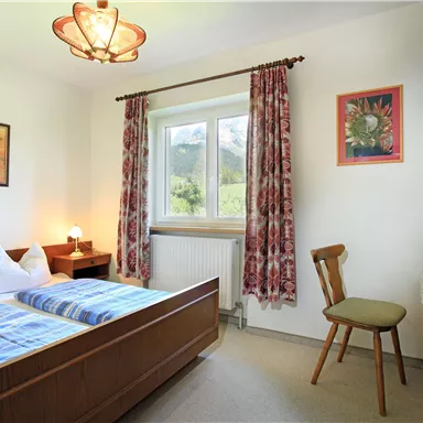 Ein gemütliches Schlafzimmer mit zwei Betten und einer hellen Fensterfront. Der Raum ist einfach eingerichtet und verfügt über einen Fernseher und einen kleinen Tisch.