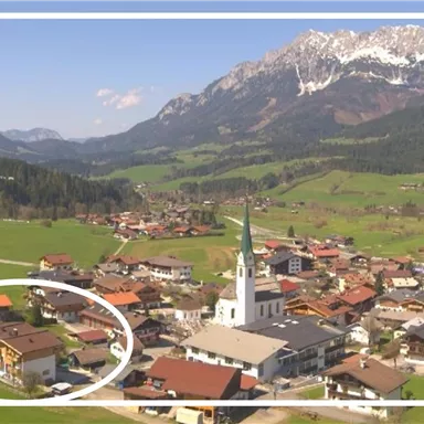 Eine malerische Landschaft mit einem kleinen Dorf, umgeben von Bergen. Im Vordergrund steht eine Kirche und einige Häuser am Fuße der Berge.