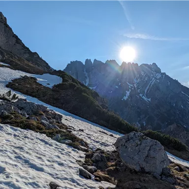 Eine verschneite Berglandschaft mit steilen Felsen und strahlendem Sonnenschein. Der Himmel ist klar und blau.