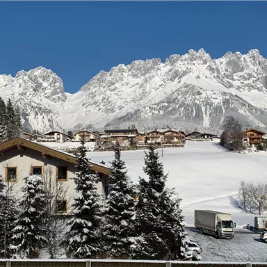Eine malerische Winterlandschaft mit schneebedeckten Bergen und traditionellen Chalets. Der klare blaue Himmel ergänzt die ruhige Atmosphäre der Umgebung.