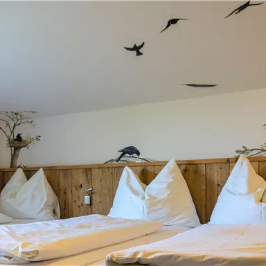 Ein gemütliches Zimmer mit weißen Bettdecken und Kissen. An der Wand sind Vögel und ein Baum dekorativ angebracht.