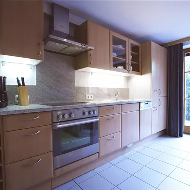 A modern kitchen with wooden cabinets and a stainless steel sink. Large windows provide plenty of daylight.