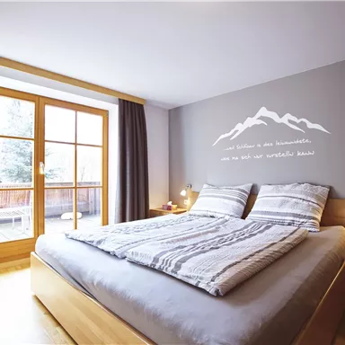 A bright bedroom with a large bed and wooden details. Large windows provide a view outside and create an inviting atmosphere.