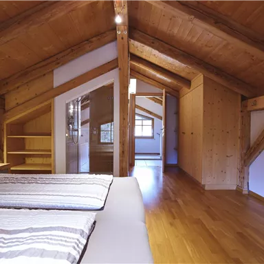 A cozy room in the attic with wooden ceilings and a modern design. It features a double bed and plenty of storage space.