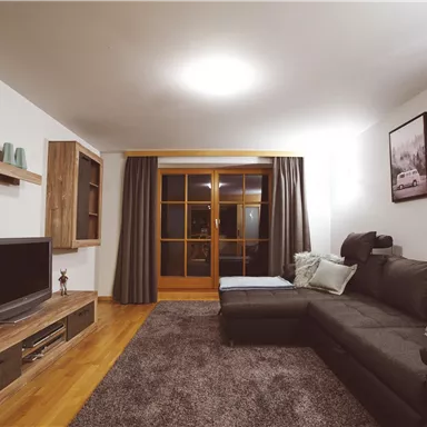 A modern living room with a cozy sofa and a television. Large windows and wooden shelves create an inviting atmosphere.