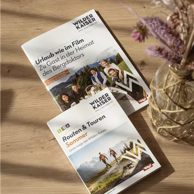 Zwei Broschüren auf einem Holztisch. Die Titel thematisieren Urlaub und Wanderungen im Wilder Kaiser Gebiet.