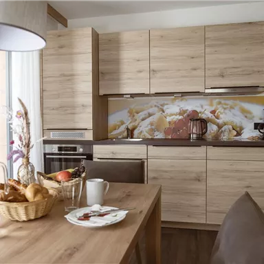 Eine moderne Küche mit Holzschränken und einem Essbereich. Auf dem Tisch sind frisches Brot, Geschirr und ein Glas Wasser zu sehen.