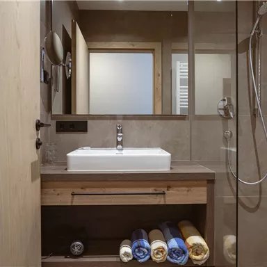 Ein modernes Badezimmer mit einem Waschbecken und einer Dusche. Handtücher sind ordentlich im Schrank gestapelt.