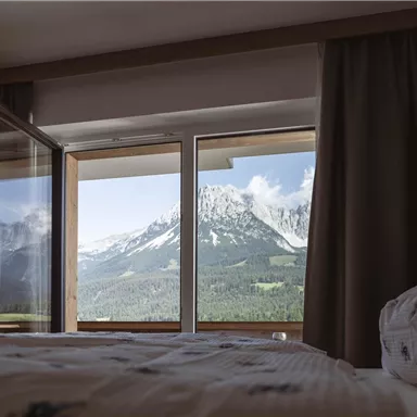 Ein gemütliches Schlafzimmer mit Blick auf majestätische Berge. Das Fenster öffnet sich zu einer schönen Landschaft mit klarer Aussicht.