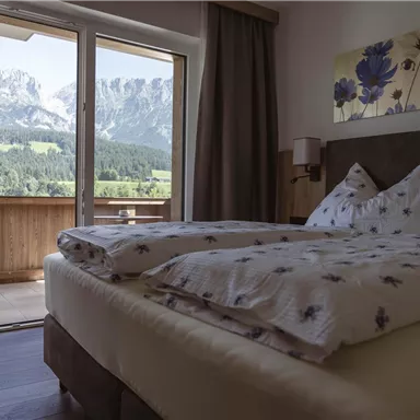 Ein gemütliches Schlafzimmer mit einem Doppelbett und einer schönen Aussicht auf die Berge. Große Fenster bieten Zugang zu einem Balkon mit Blick auf die Natur.