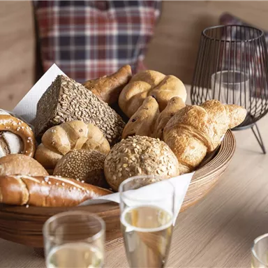 Ein hübsches Tablett mit verschiedenen Brötchen und Gebäck. Im Hintergrund sind Gläser und eine Banane zu sehen.