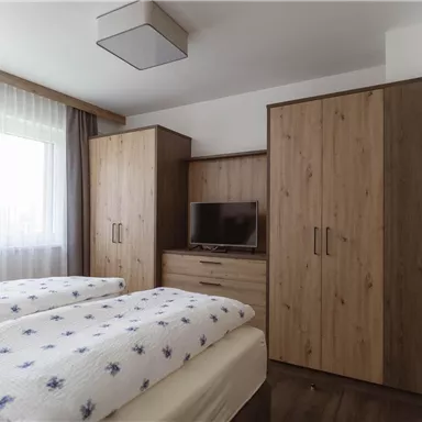 Ein gemütliches Schlafzimmer mit zwei Einzelbetten, einem Holzschrank und einem Fernseher. Das Fenster sorgt für viel Tageslicht.