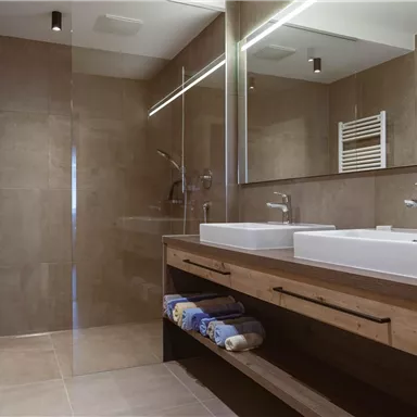 Ein modernes Badezimmer mit einer geräumigen Dusche und zwei Waschbecken. Die Wände sind in neutralen Tönen gehalten und das Mobiliar ist aus Holz.