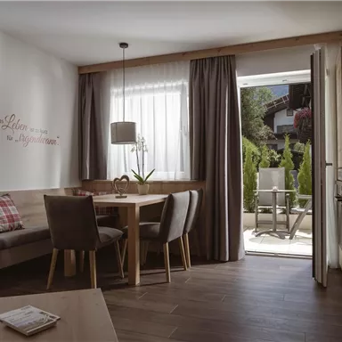 Ein gemütliches Wohnzimmer mit einem Essbereich und großen Fenstern. Der Raum hat einen warmen, einladenden Holzlook und Zugang zu einer Terrasse.