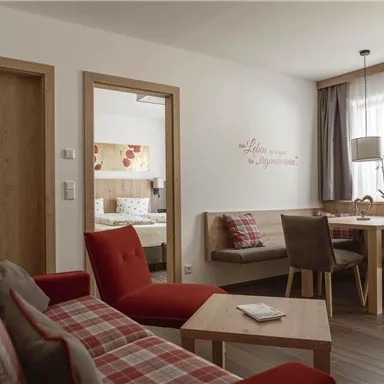 Ein gemütlicher Wohnraum mit rot karierten Sofas und einem Holztisch. Das Zimmer ist hell und einladend, mit einem großen Fenster, das Tageslicht hereinlässt.