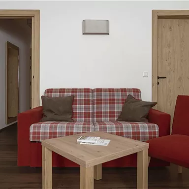 Ein gemütliches Wohnzimmer mit einem roten Sofa und einem roten Sessel. Der Holztisch ergänzt die freundliche Atmosphäre des Raumes.