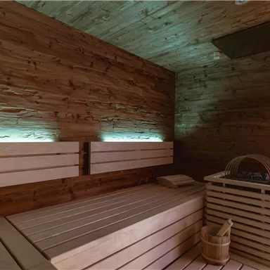 Eine gemütliche Sauna mit Holzverkleidung und sanftem, grünem Licht. Die Bänke und der Eimer sind bereit für Entspannung.