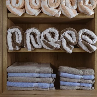 Rollenförmige Handtücher auf einem Holzregal. Die farbigen Handtücher sind ordentlich gestapelt und verleihen eine gemütliche Atmosphäre.