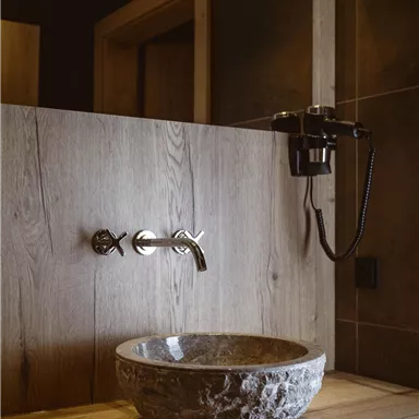 Ein modernes Badezimmer mit einer eleganten Steinwaschschüssel und einer stylischen Armatur. Die Wände sind in warmen Holztönen gehalten, was eine gemütliche Atmosphäre schafft.